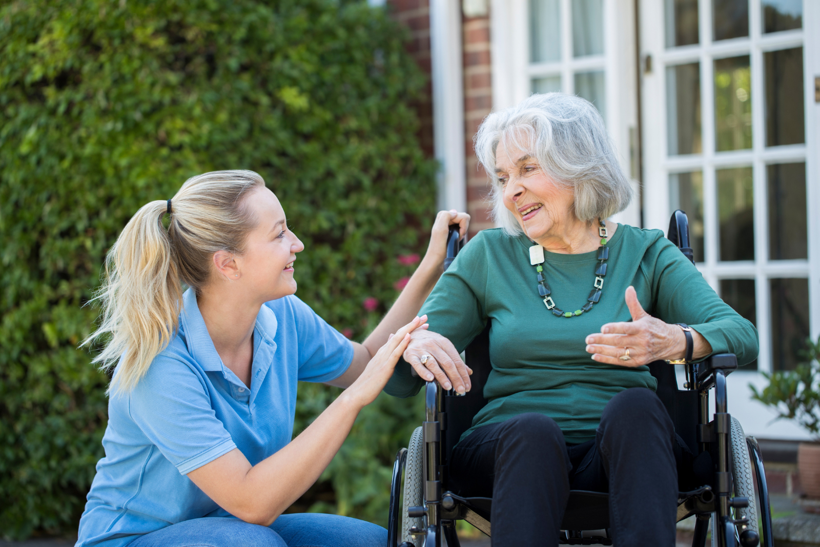 A caregiver talking to an older client in a wheelchair represents quality dementia home care services in Norwell