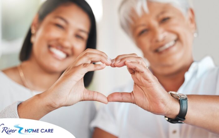 A daughter and an older mother create a heart with their hands, representing the feeling that is highlighted during National Family Caregivers Month