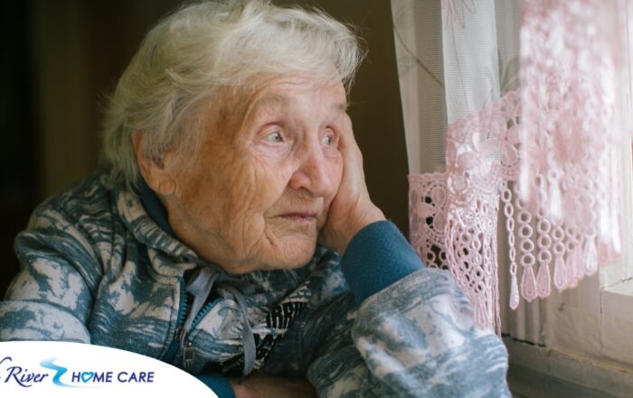 An older woman peacefully looks out of the window while the sun is still up, representing what can happen with sundowning.