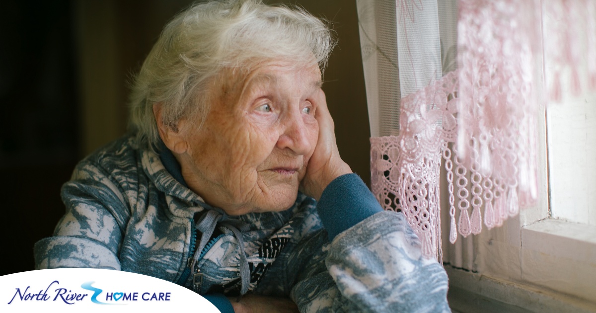 An older woman peacefully looks out of the window while the sun is still up, representing what can happen with sundowning.