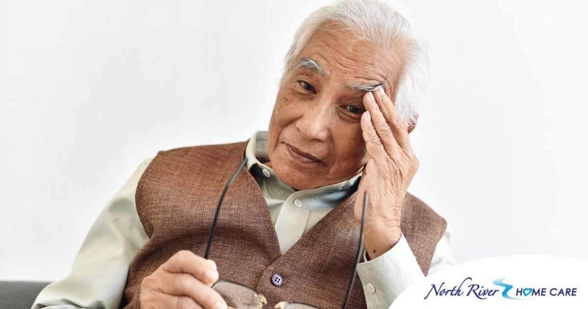 An older adult holds his head and his glasses representing vision problems like macular degeneration.