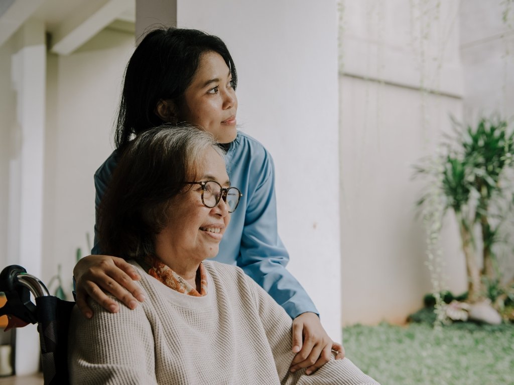 A cheerful caregiver gently embraces an elderly woman in a wheelchair as they both look outside with warm smiles. The image reflects compassionate and personalized senior home care in Chatham, highlighting connection, comfort, and trust.