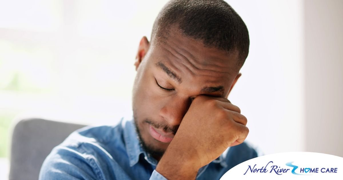 A man tiredly rubs his eyes, representing the exhaustion that can come with family caregiving.