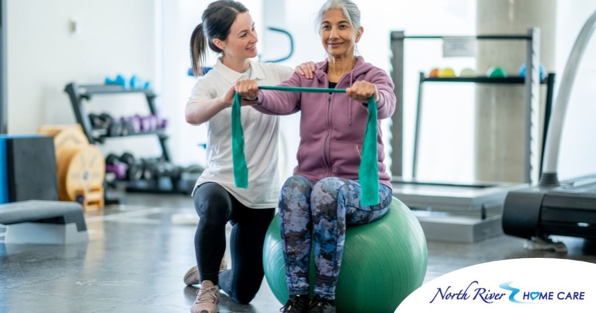 A care provider helps an older woman exercise with a resistance band and an exercise ball, representing how exercise can help with senior fall prevention.