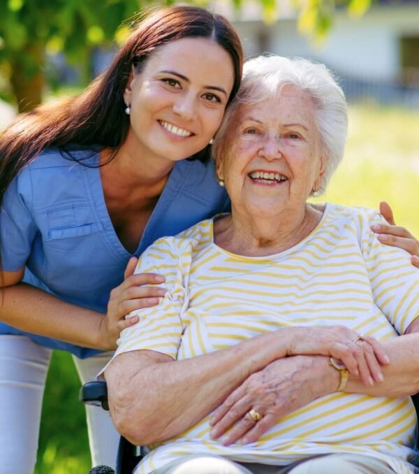 A smiling caregiver hugging a happy older woman outdoors